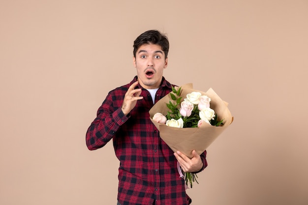 Front view young male holding beautiful flowers on brown wall