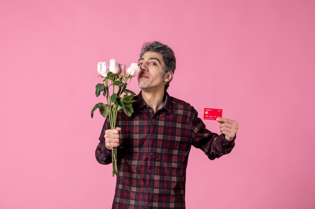 Front view young male holding beautiful pink roses and bank card on pink wall