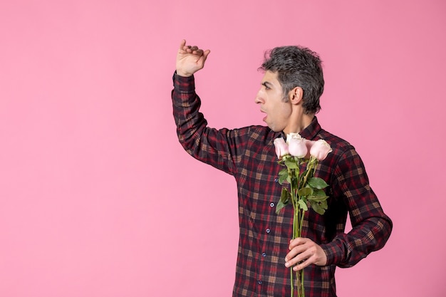 Front view young male holding beautiful pink roses on pink wall