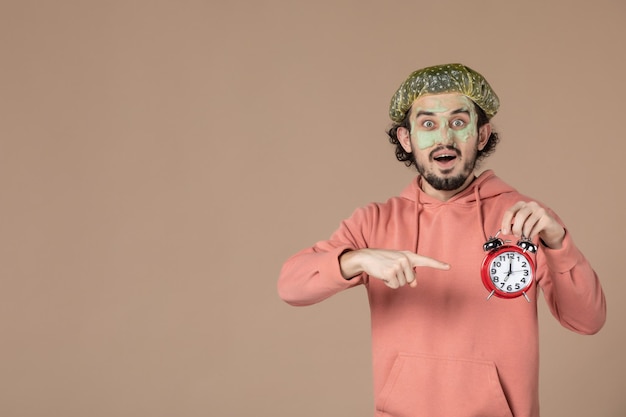 front view young male holding clocks on a brown background spa money therapy salon facial skin bodycare