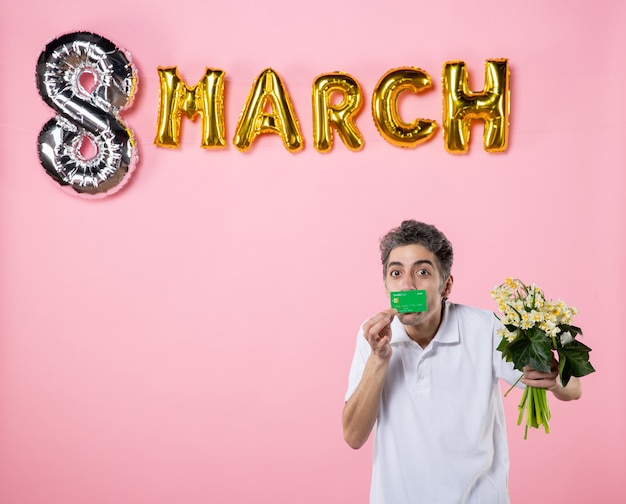 Photo front view young male holding flowers for woman and bank card with march decorated pink background emotion womens day equality party glamour feminine holiday