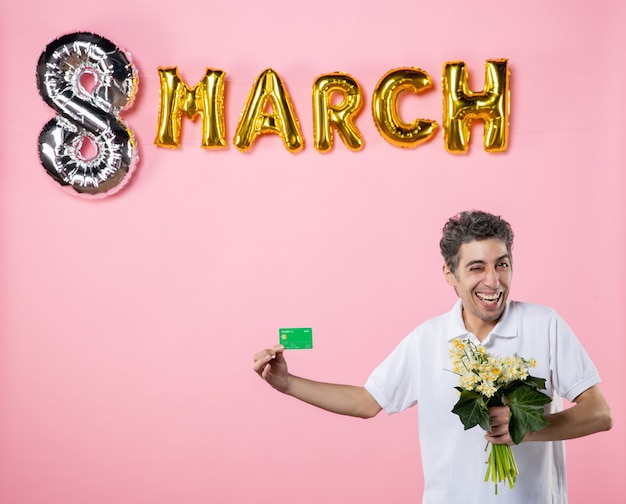 front view young male holding flowers for woman and bank card with march decorated pink background sensual emotion womens day equality party glamour feminine holidays