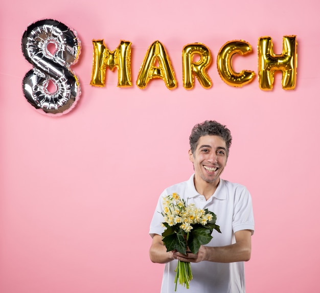 Photo front view young male holding flowers for woman with march decorated pink background equality party sensual holiday womens day emotion glamour color