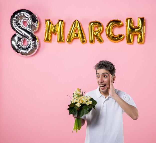 Photo front view young male holding flowers for woman with march decorated pink background equality party sensual womens day glamour color holiday emotion