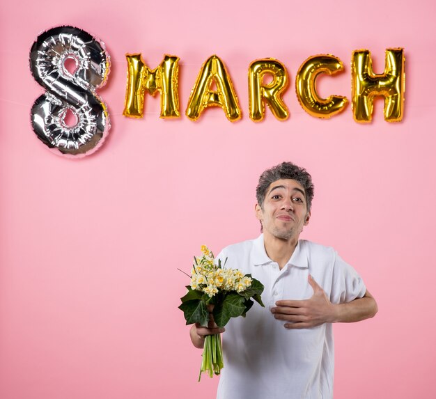 Photo front view young male holding flowers for woman with march decorated pink background equality sensual holiday womens day party emotion glamour color