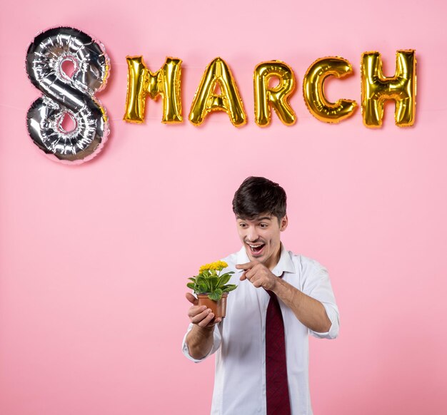 Front view young male holding little flower in pot with march decoration on pink background color present man equality womens day party marriage