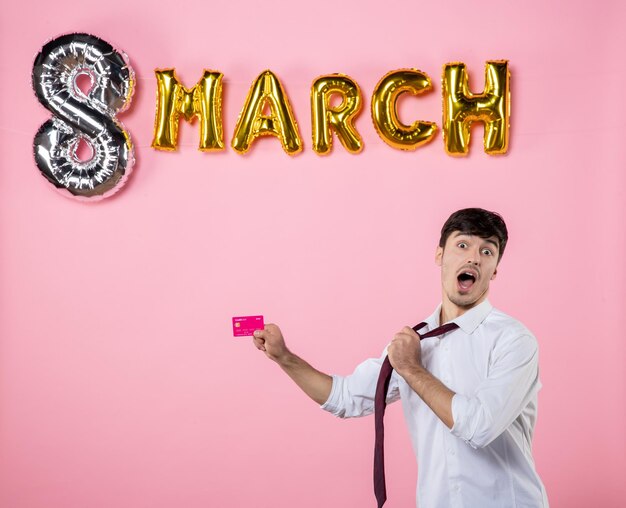 Front view young male holding pink bank card with march decoration on pink background feminine color money party holiday shopping man present