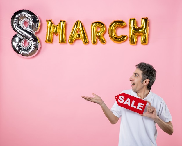 front view young male holding red sale nameplate with march decorated pink background equality party present glamour shopping