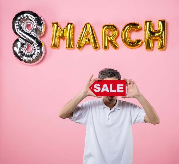 Photo front view young male holding red sale nameplate with march decorated pink background sensual glamour love mall present money equality party