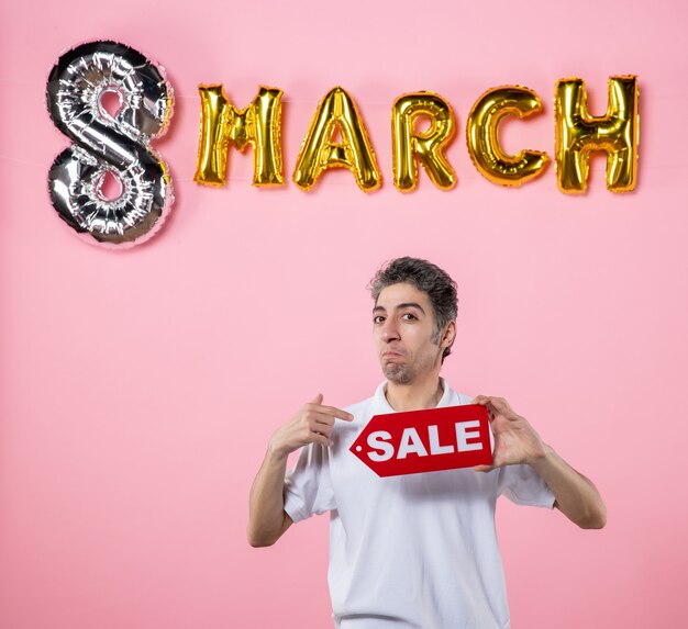 front view young male holding red sale nameplate with march decorated pink background sensual glamour marriage love mall present money equality party