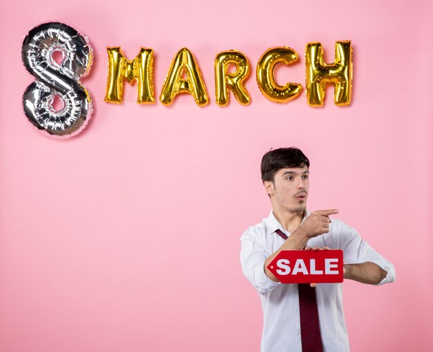 Front view young male holding red sale nameplate with march decoration on pink background color holiday party feminine equality money man present