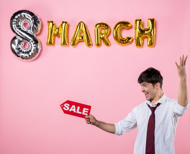 Front view young male holding red sale nameplate with march decoration on pink background party feminine shopping man present holiday color equality money