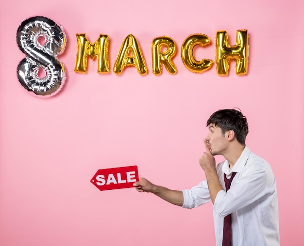 Front view young male holding red sale nameplate with march decoration on pink background party feminine shopping present holiday color equality money man