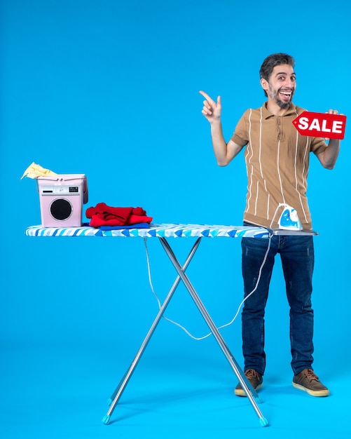 front view young male holding red sale writing on blue background housework clean shopping housewife washing machine iron