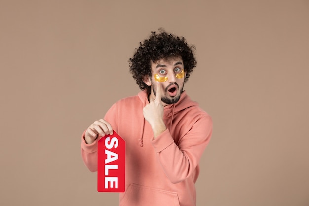 正面図茶色の背景に販売ネームプレートを保持している若い男性フェイシャルサロンスキンセラピースパスキンケアマッサージ