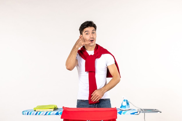 Front view young male behind ironing board asking to call on white wall man home work clean effort emotion housework fashion clothes