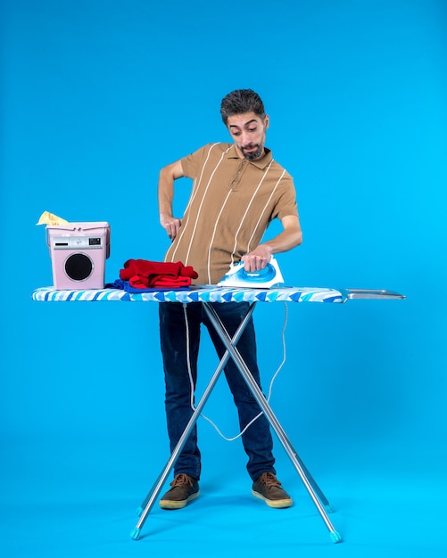 Photo front view young male ironing behind board on blue background color housework clean laundry man machine wash emotion