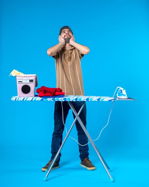 front view young male behind ironing board on blue background color housework laundry clean washing machine emotion