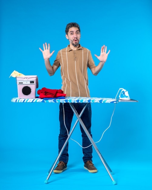 front view young male behind ironing board on a blue background color housework laundry man clean wash machine emotion