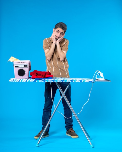 front view young male behind ironing board on blue background color housework laundry man washing machine emotion