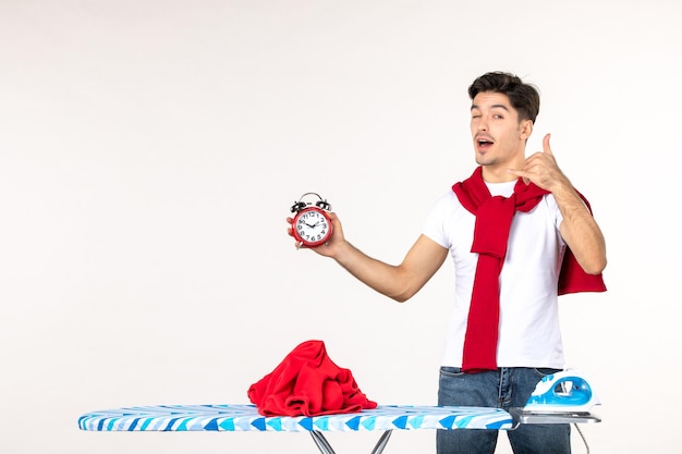 Front view young male behind ironing board holding clocks on white background laundry home work housework clean emotion time man color