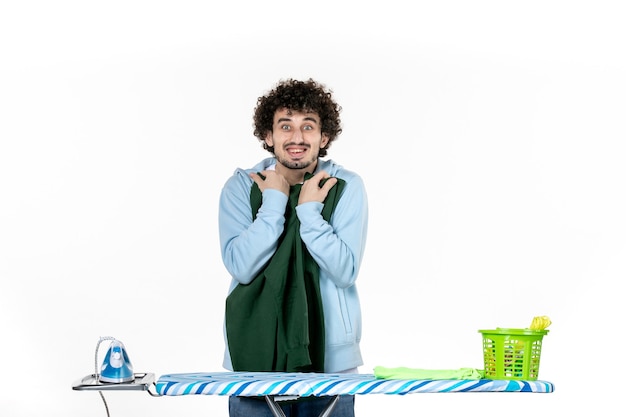 вид спереди молодой мужчина за гладильной доской держит зеленую рубашку на белом фоне работа по дому гладильная цветная стирка одежды чистка эмоция мужчина
