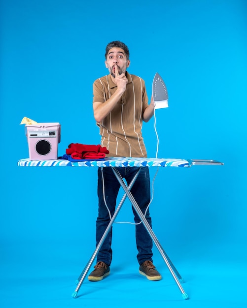 Photo front view young male behind ironing board holding iron on a blue background color housework clean man laundry emotion wash machine