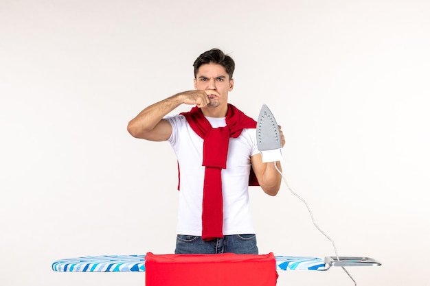 Front view young male behind ironing board holding iron on white