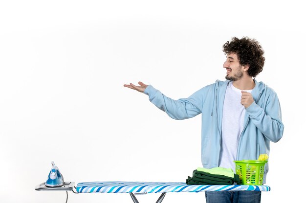 front view young male behind ironing board on the white background color man cleaning housework laundry photo iron clothes