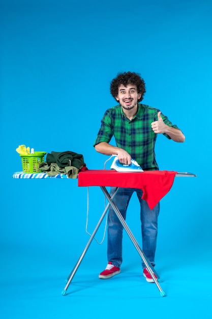 front view young male ironing red clothes on board on blue background color house washing machine human clean