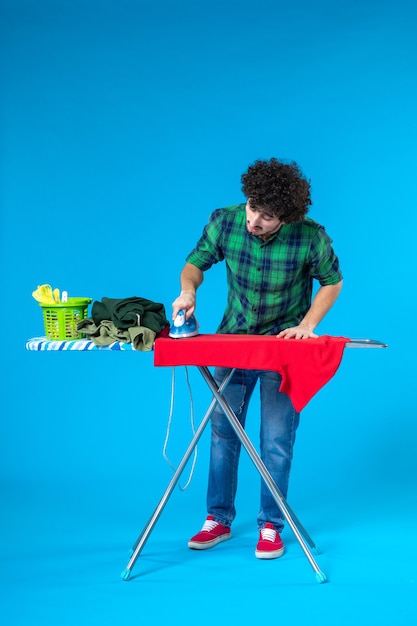 front view young male ironing red shirt on board on blue background clean washing machine housework house color human
