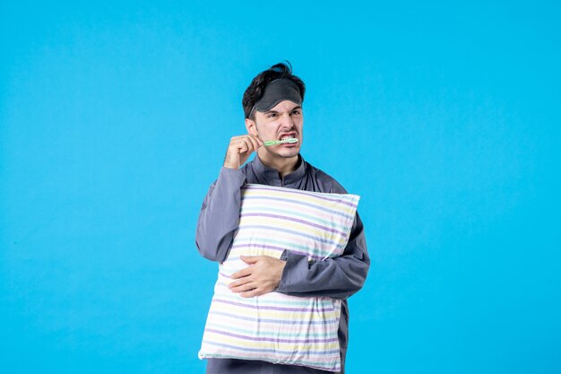 front view young male in pajamas brushing his teeth before sleep on blue background late color rest human wake bed night dream sleep