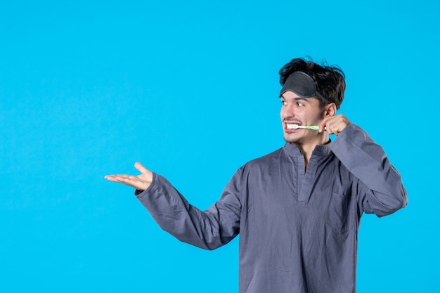 front view young male in pajamas cleaning his teeth on blue background color rest night wake dream nightmare human bed dark