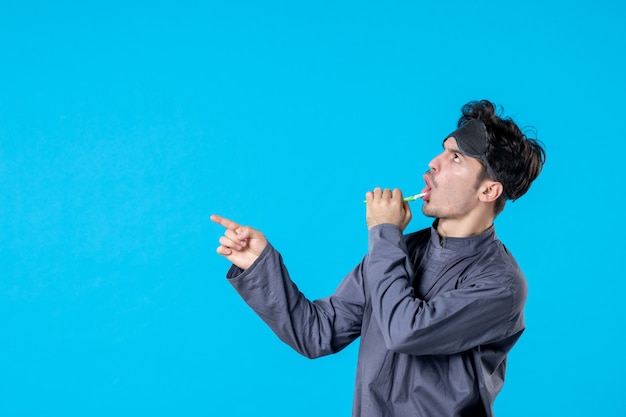 front view young male in pajamas cleaning his teeth on blue background color rest night wake nightmare human dark pillow dream