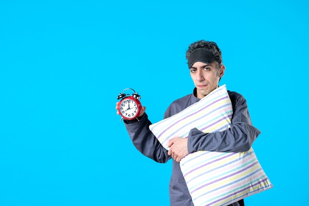 front view young male in pajamas holding pillow and clocks on blue background nightmare dream bedroom insomnia sleep rest dark night bed