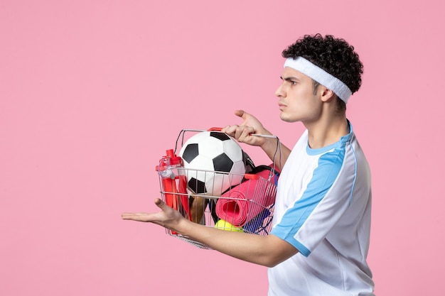 Front view young male in sport clothes with basket full of sport things pink wall