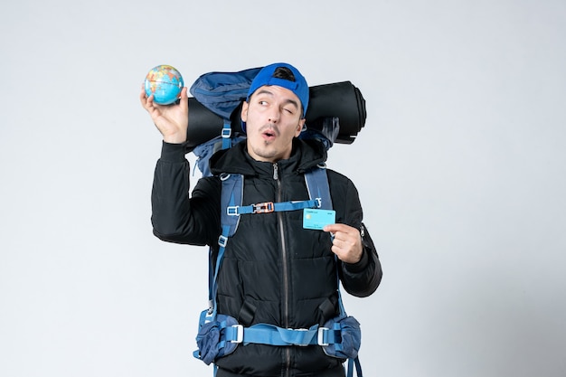 front view young male with backpack holding earth globe and bank card on white background air money mountain campaign forest nature snow camp