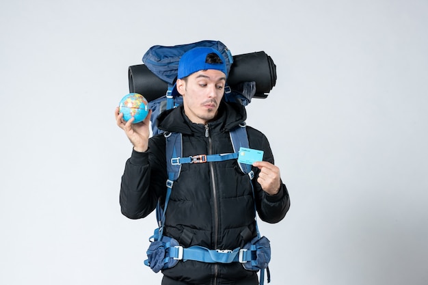 front view young male with backpack holding earth globe and bank card on white background campaign air money forest nature cold mountain camp