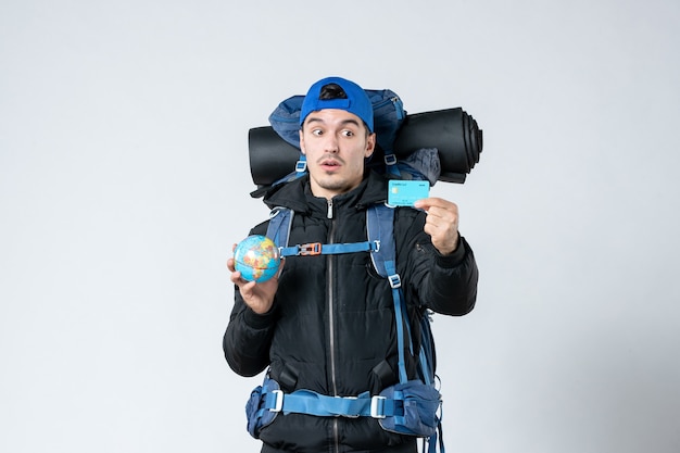 front view young male with backpack holding earth globe and bank card on white background money mountain campaign air snow nature cold camp