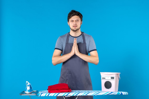 Вид спереди молодой мужчина с гладильной доской на синем фоне, работа по дому, утюг, прачечная, чистка, стиральная машина, цвет человека