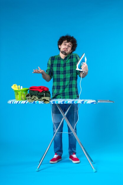 Front view young male with ironing board holding iron on a blue\
background color house washing machine clean housework human