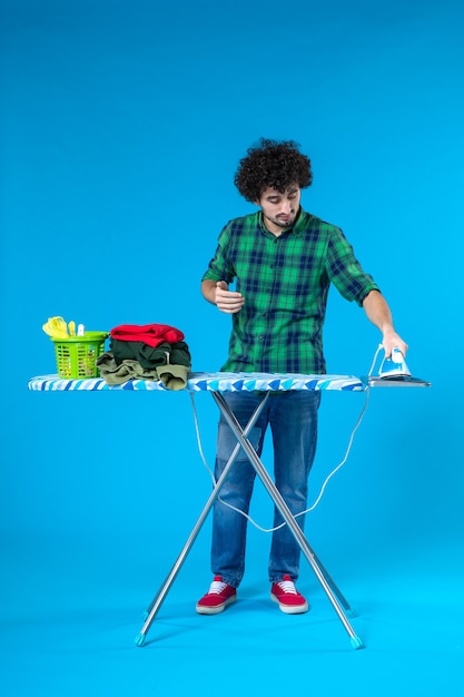 Front view young male with ironing board putting iron into its place on blue background house clothes washing machine housework clean human