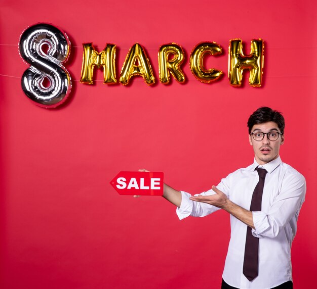 front view young male with march decoration holding sale nameplate on red background shopping woman womans day present colors sensual holiday vogue