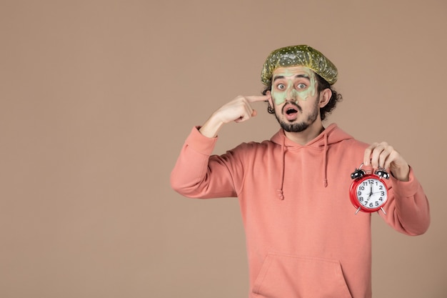 front view young male with mask holding clocks on brown background skin spa therapy time bodycare facial