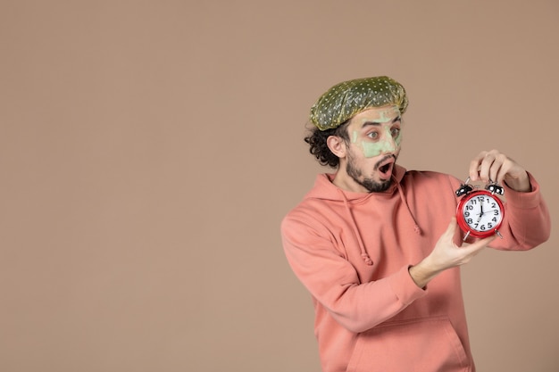 front view young male with mask holding clocks on brown background therapy time salon skin bodycare facial