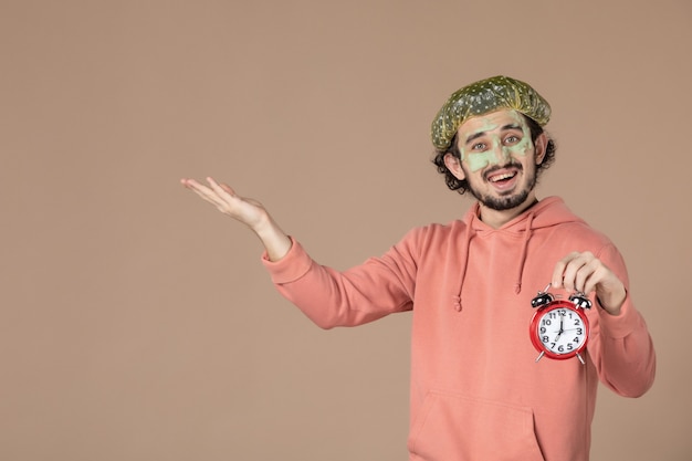 front view young male with mask holding clocks on brown background time skin spa therapy bodycare facial