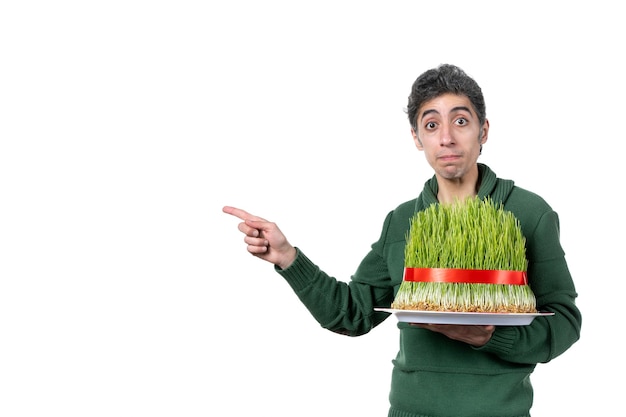 front view of young man holding big novruz semeni tied with red bow on white wall