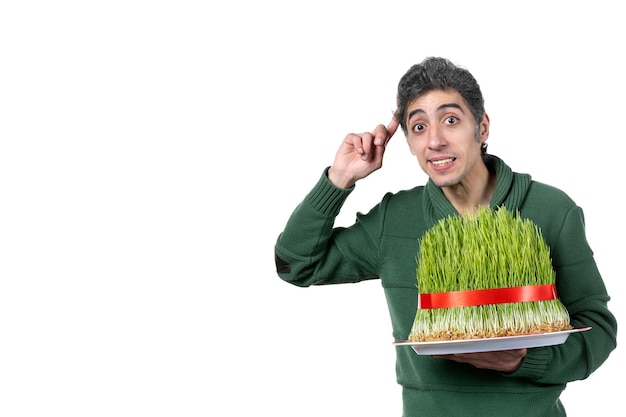 front view of young man holding big novruz semeni tied with red bow on white wall