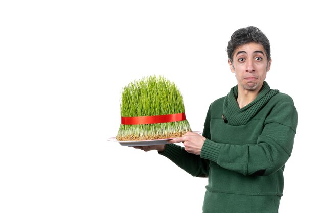 front view of young man holding big novruz semeni tied with red bow on white wall