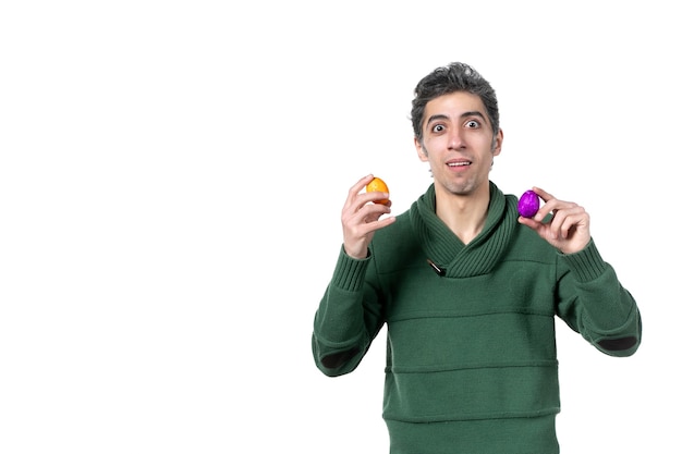 front view of young man holding colored painted eggs on white wall